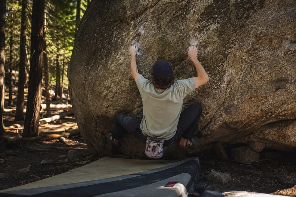 Grimpeur de bloc de dos accroupi sur un rocher en forêt, tapis de réception au sol