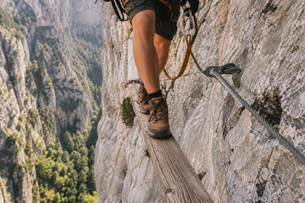 Passage sur une poutre en bois suspendue le long d'une via ferrata en falaise calcaire