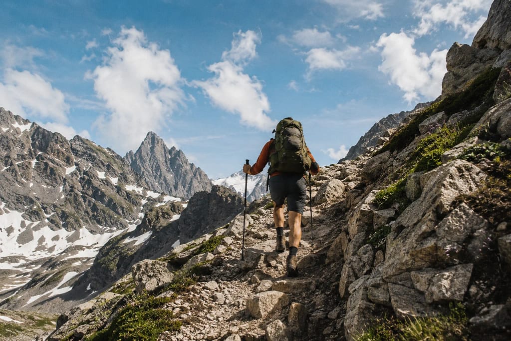 Randonneur de dos gravissant un sentier rocheux escarpé en haute montagne pyrénéenne