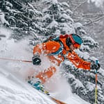Un skieur en tenue orange plonge dans une neige fraîchement tombée.