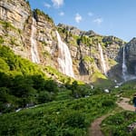 Famille en randonnée sur un sentier du Cirque du Fer-à-Cheval, entourée de majestueuses cascades et de montagnes verdoyantes.