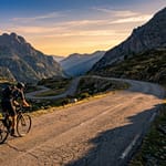 L'ascension mythique du Col du Portet depuis Saint-Lary Cycliste sur la route sinueuse du Col du Portet au coucher du soleil, entouré de montagnes pyrénéennes escarpées.
