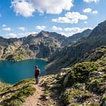 Randonnée au lac du Montagnon : l'itinéraire vers le cœur Randonneur contemplant le lac du Montagnon, un lac bleu profond en forme de cœur niché entre des montagnes rocheuses sous un ciel clair.