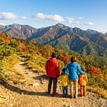 Partir à la découverte des montagnes du Japon en famille Famille de dos admirant un vaste paysage montagneux japonais en automne, avec le Mont Fuji enneigé à l'horizon.