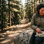 Femme souriante mangeant des noix pendant une pause de randonnée en forêt
