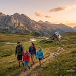 Famille en randonnée marchant sur un sentier montagneux vers un refuge au coucher du soleil dans les Pyrénées.