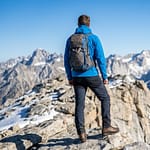 Un randonneur équipé d'un sac à dos regarde des sommets enneigés depuis le sommet d'une montagne.