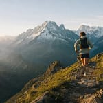 Coureur de trail vu de dos sur un sentier alpin avec sommets enneigés en arrière-plan