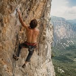Grimpeur de dos en pleine ascension sur une paroi rocheuse ensoleillée