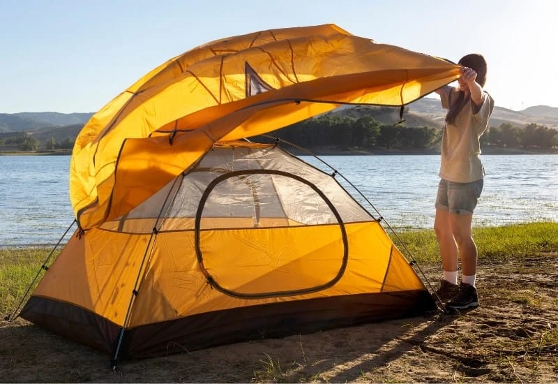 une femme installe une tente près d'un lac